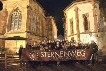 Viele Menschen halten ein Plakat mit dem Titel Sternenweg vor eine Kirche